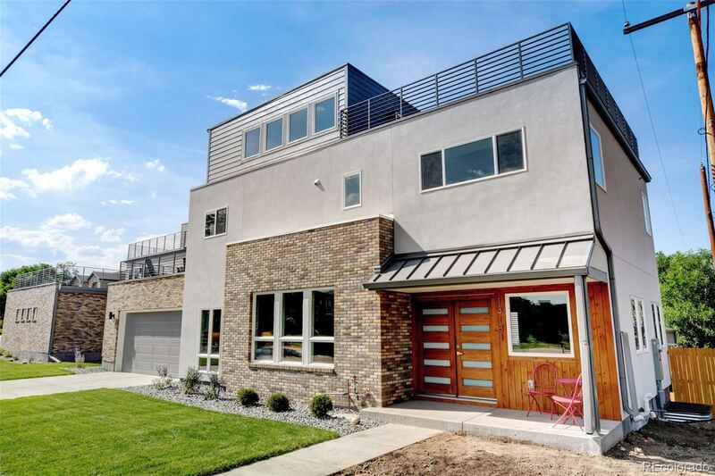Modern two-story home with brick accents, metal roof, and rooftop deck, set against a blue sky.