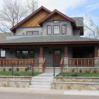 Two-story Craftsman house with gray siding, wood trim, and a front porch with a stone wall and wrought iron fence.