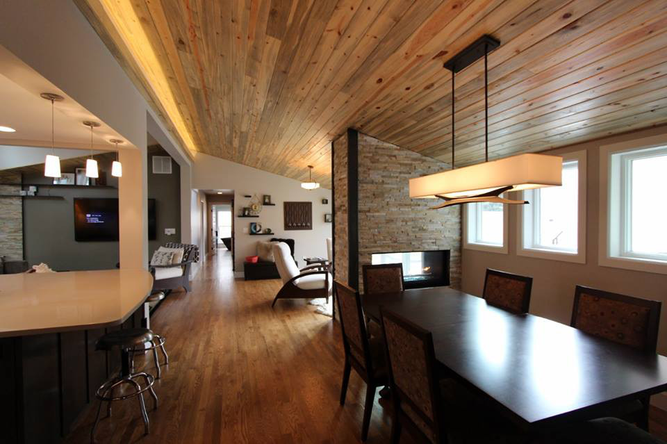 Dining room with wooden ceiling and floor, dark table and chairs, fireplace, and windows.