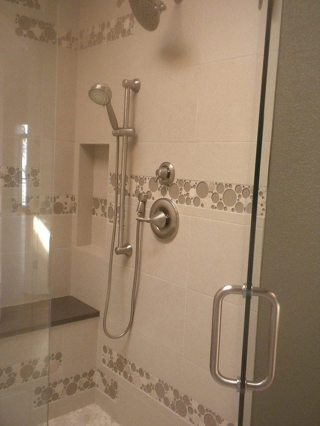 Shower with white and tan tiles, chrome fixtures, glass door, and built-in bench.