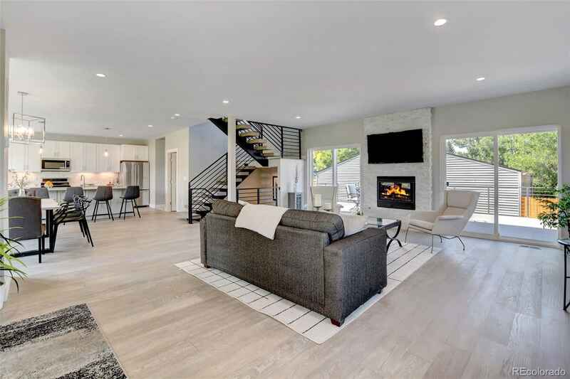 Open-plan living space with kitchen, living room, fireplace, and spiral staircase. Neutral tones, modern design.