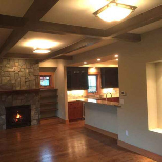 Living room with a fireplace, kitchen pass-through, hardwood floors, and wood beam ceiling.