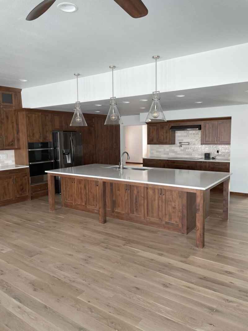 Spacious kitchen with a large island, dark wood cabinets, light countertops, and three pendant lights.
