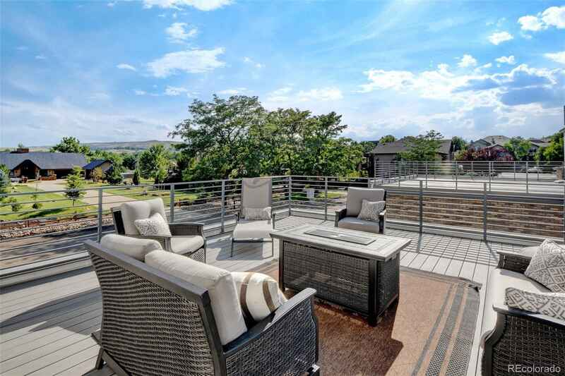 Outdoor deck with patio furniture, including a fire pit, overlooking a landscape under a bright blue sky.