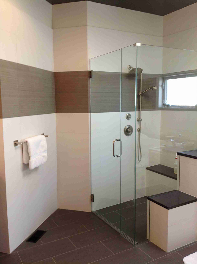 Modern bathroom with a glass shower, brown tiles, and a white towel.