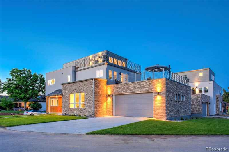 Modern multi-story home with brick and white siding, garage, and rooftop patio under a blue sky.