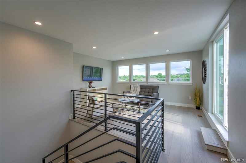 Modern loft space with staircase and sitting area, featuring a TV, large windows, and minimalist decor.