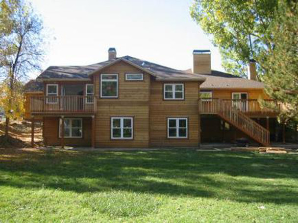Two-story wooden house with decks and windows in a grassy yard.