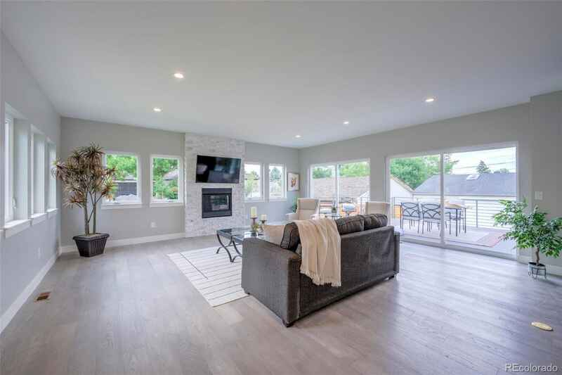 Spacious, modern living room with gray walls, hardwood floors, and a fireplace. Includes large windows and a gray sofa.