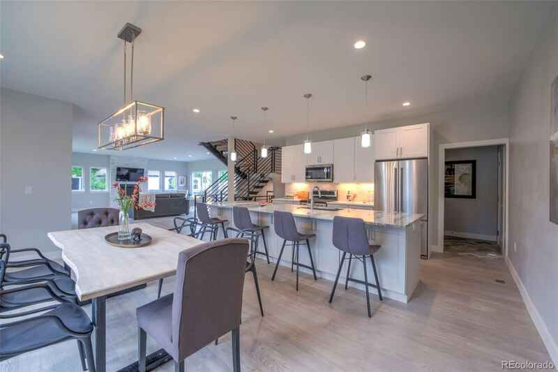 Modern kitchen with a dining table, a kitchen island, and a staircase, featuring light gray walls and wooden floors.
