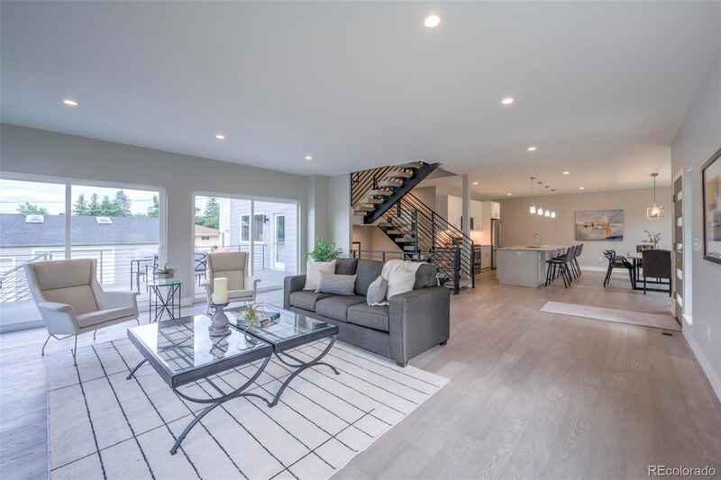 Open-concept living area with gray sofa, modern staircase, and large windows overlooking a patio.