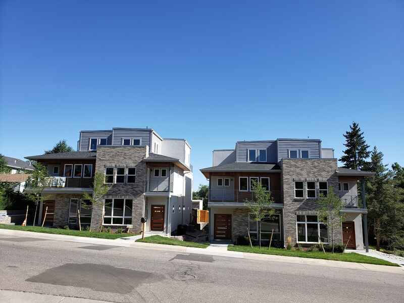 Two modern townhouses with stone and wood accents on a sunny street.