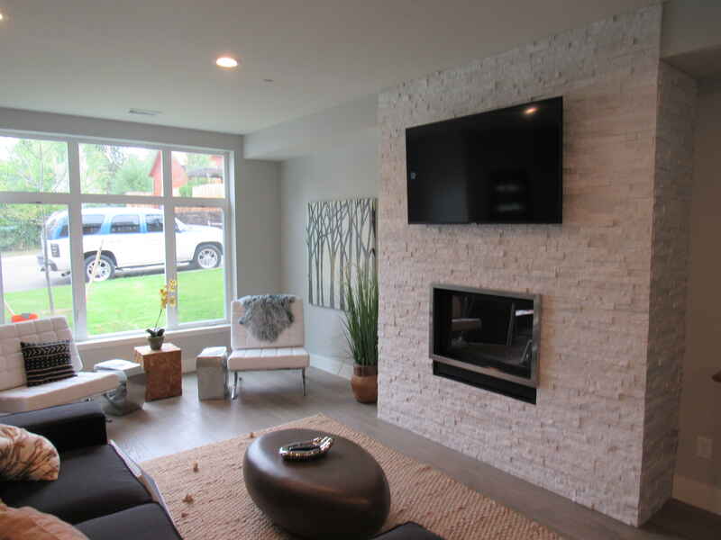 Modern living room with white stone fireplace and large TV. A black sofa and chairs surround a round coffee table.