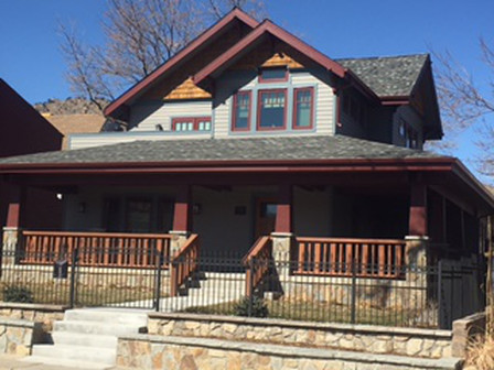 Two-story Craftsman home with stone accents, porch, and railings. Gray siding, dark red trim, and clear blue sky.