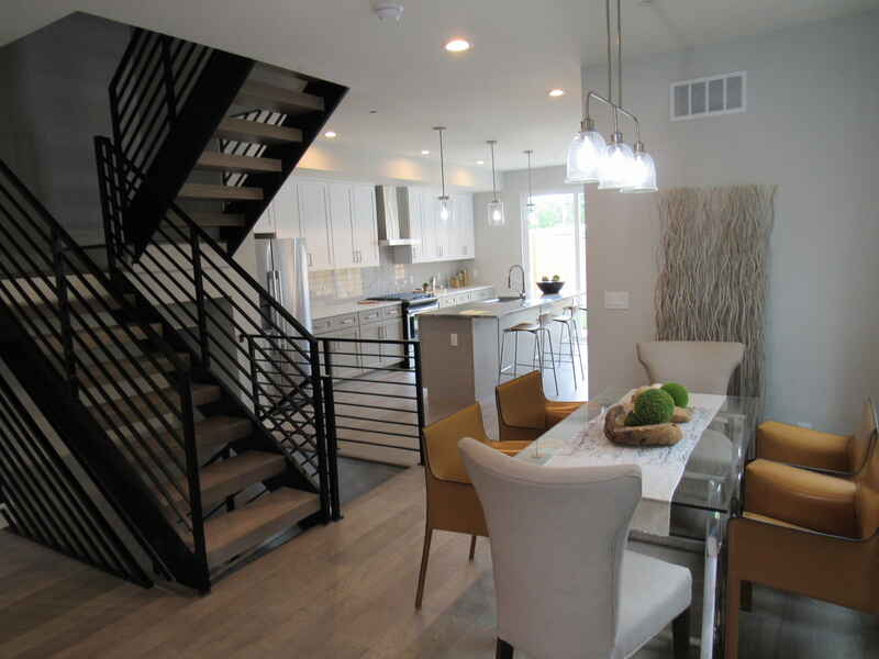 Modern dining area with staircase, kitchen in background; yellow and white chairs, glass table.