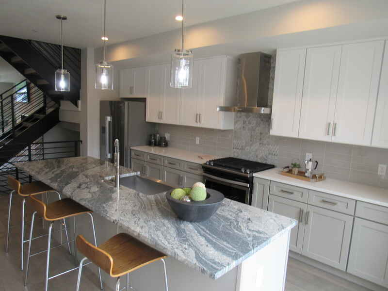 Modern kitchen with gray granite island, white cabinets, stainless steel appliances, and bar stools.