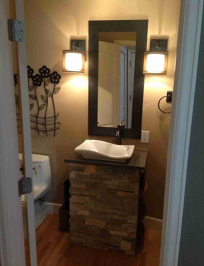 Powder room with stone-faced sink base, vessel sink, square mirror, sconces, and decorative wall art.