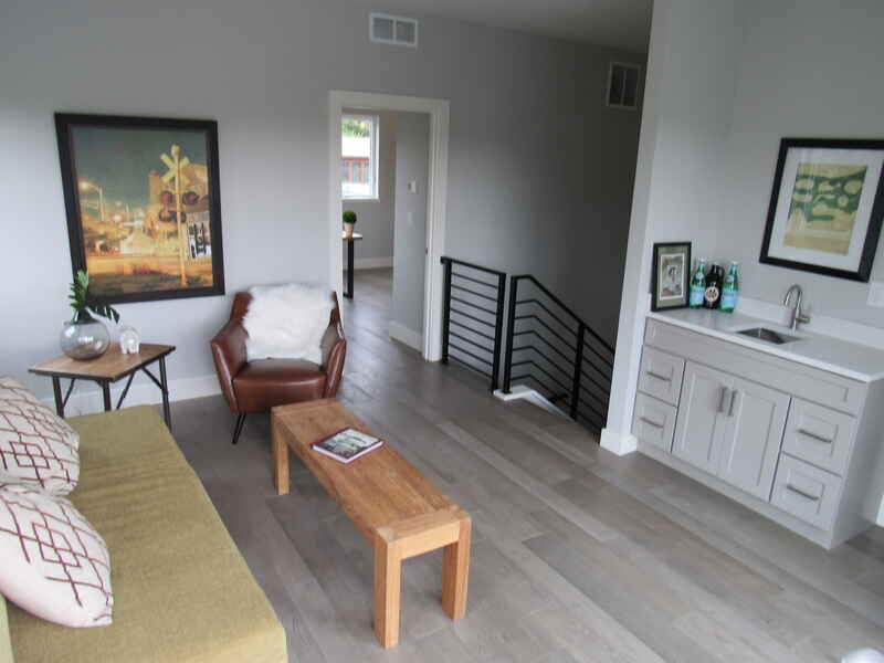 Living room with gray walls, light wood floor, seating, artwork, a bar area, and a staircase.