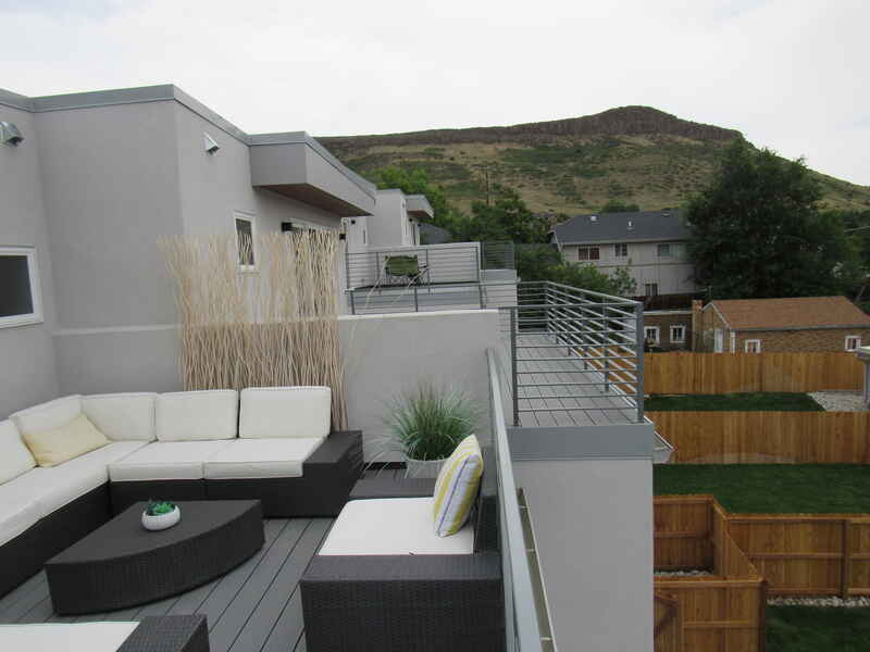Rooftop patio with modern gray furniture, overlooking houses and a mountain.
