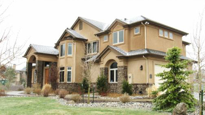 Beige two-story house with brown stone accents, white windows, and a green lawn.