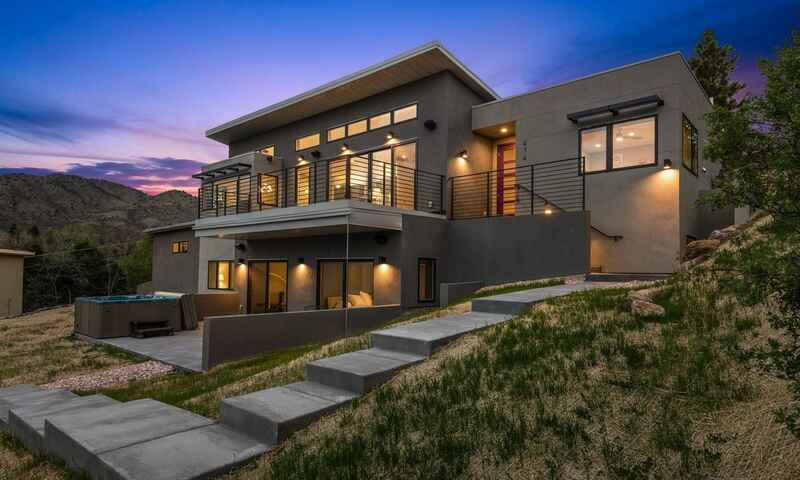 Modern two-story house with large windows and a balcony, concrete steps leading up to the home, at dusk.
