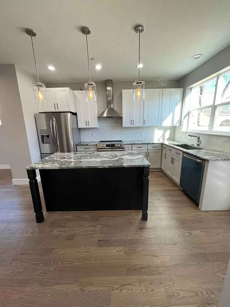Modern kitchen with white cabinets, black island, stainless steel appliances, and wood floor.