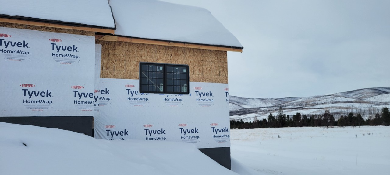 A house under construction covered in snow with a mountainous background on a cloudy day.