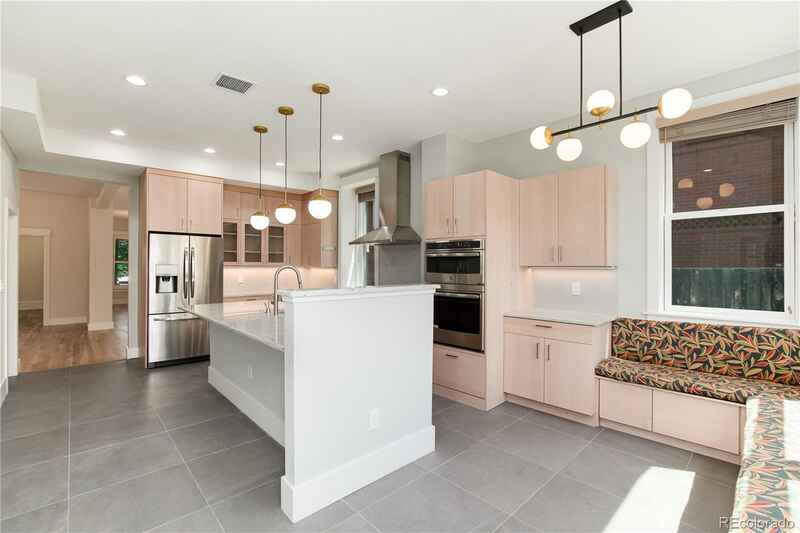 Modern kitchen with light wood cabinets, white island, gray tile, and pendant lights.