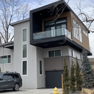 Modern two-story house with black accents, a cantilevered balcony, and a gray SUV parked in the driveway.