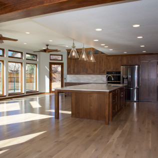 Spacious kitchen with wooden cabinets, island, and stainless steel appliances. Large windows and light wood flooring.