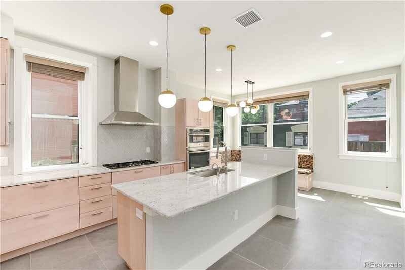 Modern kitchen with light pink cabinets, white island, stainless steel hood, and golden pendant lights.