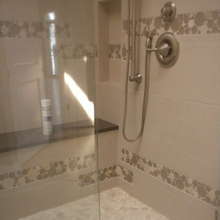 Shower with glass door, white tiles with decorative border, and stainless steel fixtures.