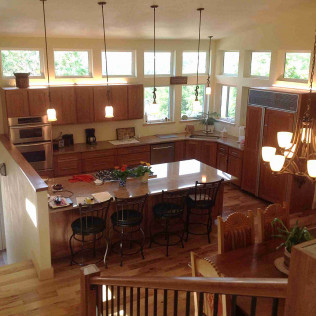 Spacious kitchen with wooden cabinets, island with stools, stainless steel appliances, and lots of natural light.
