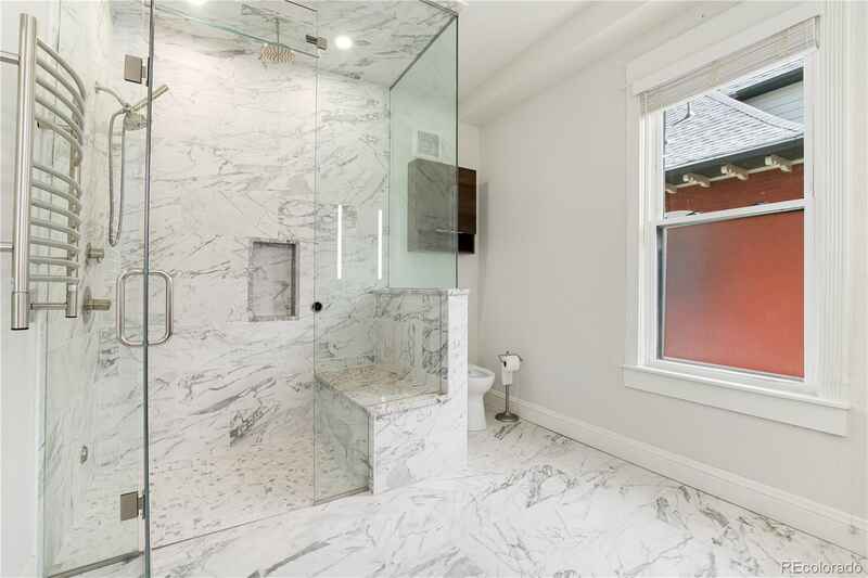 Elegant bathroom with marble shower, glass enclosure, built-in seat, and towel warmer.