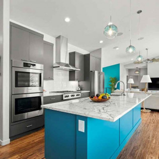 Modern kitchen with a blue island, gray cabinets, stainless steel appliances, and teal accent wall.
