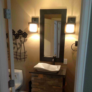 Bathroom with a stone vanity, vessel sink, mirror, wall sconces, and a toilet.