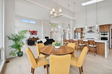 Open-concept dining area with round table and yellow chairs, connecting to kitchen and living room with bright light.