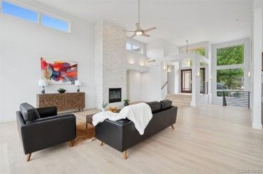 Spacious white living room with black furniture, fireplace, and large windows.