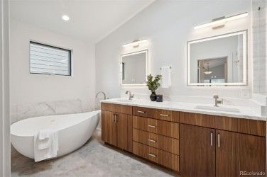 Modern bathroom with a white tub, wooden vanity with two sinks, and a large window.