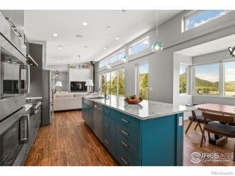 Modern kitchen with teal island, stainless steel appliances, and open to living area with views.