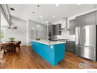 Modern kitchen with blue island, gray cabinets, stainless steel appliances, and wood floors.