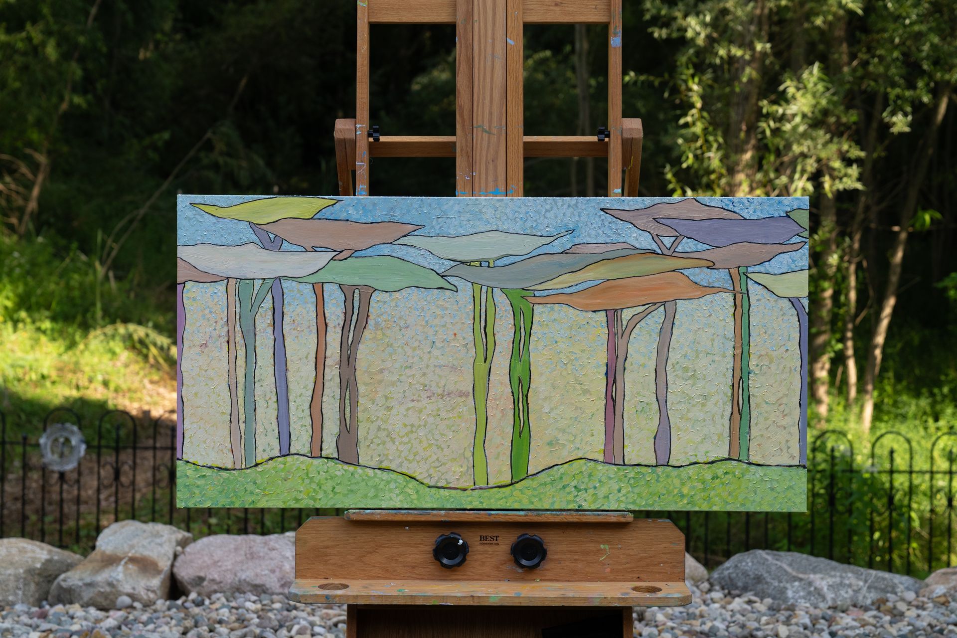 Painting of colorful trees in a garden, displayed on a wooden easel.