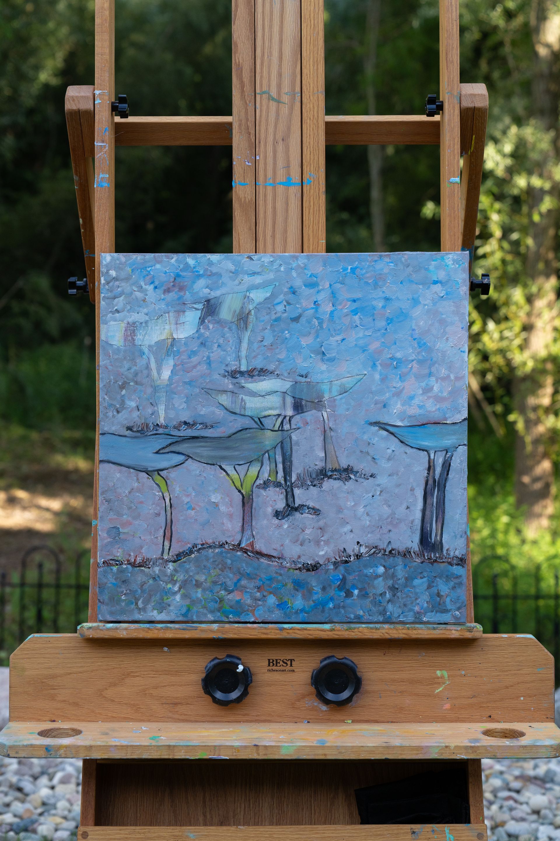 Painting of lily pads in blue and green on a wooden easel, outdoors in sunlight.