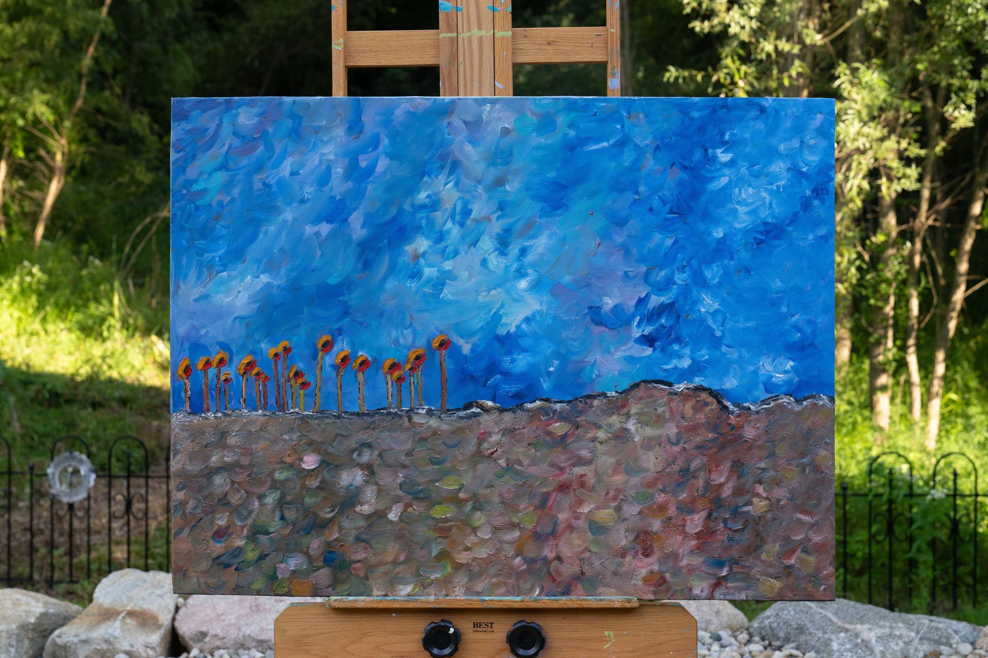 Painting of sunflowers on a landscape under a blue sky, set on an easel outdoors.