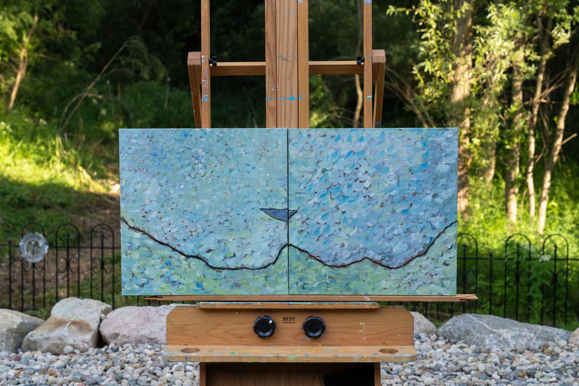 Abstract diptych painting in blues and greens on an easel outdoors, with a dark line and small triangle.