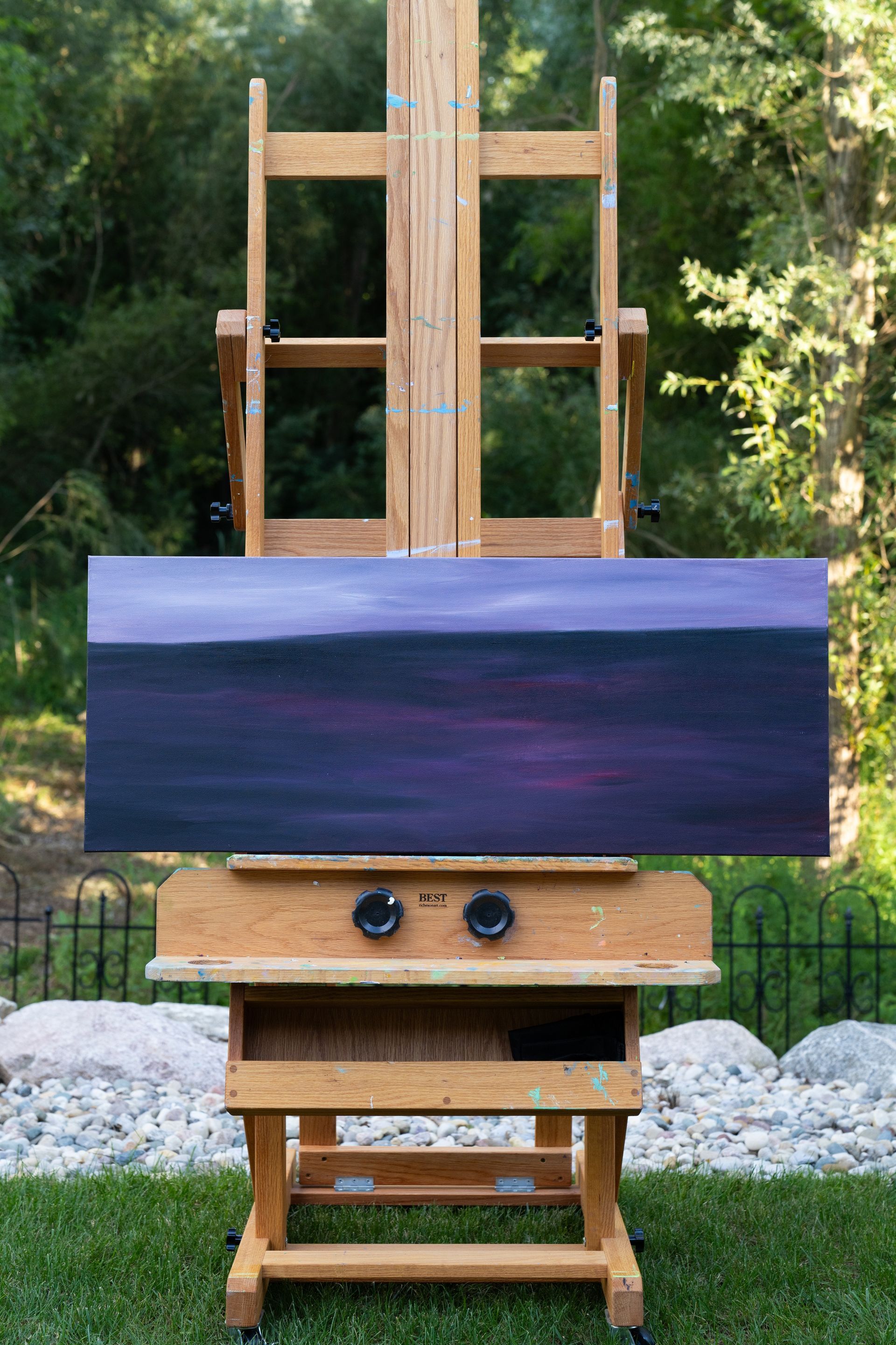 Painting on easel of a purple and pink landscape in an outdoor setting.