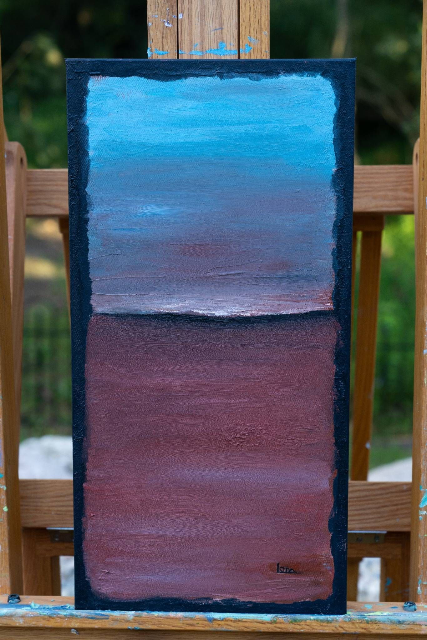Abstract painting: Blue to red gradient divided by a white line, framed in black, on an easel.