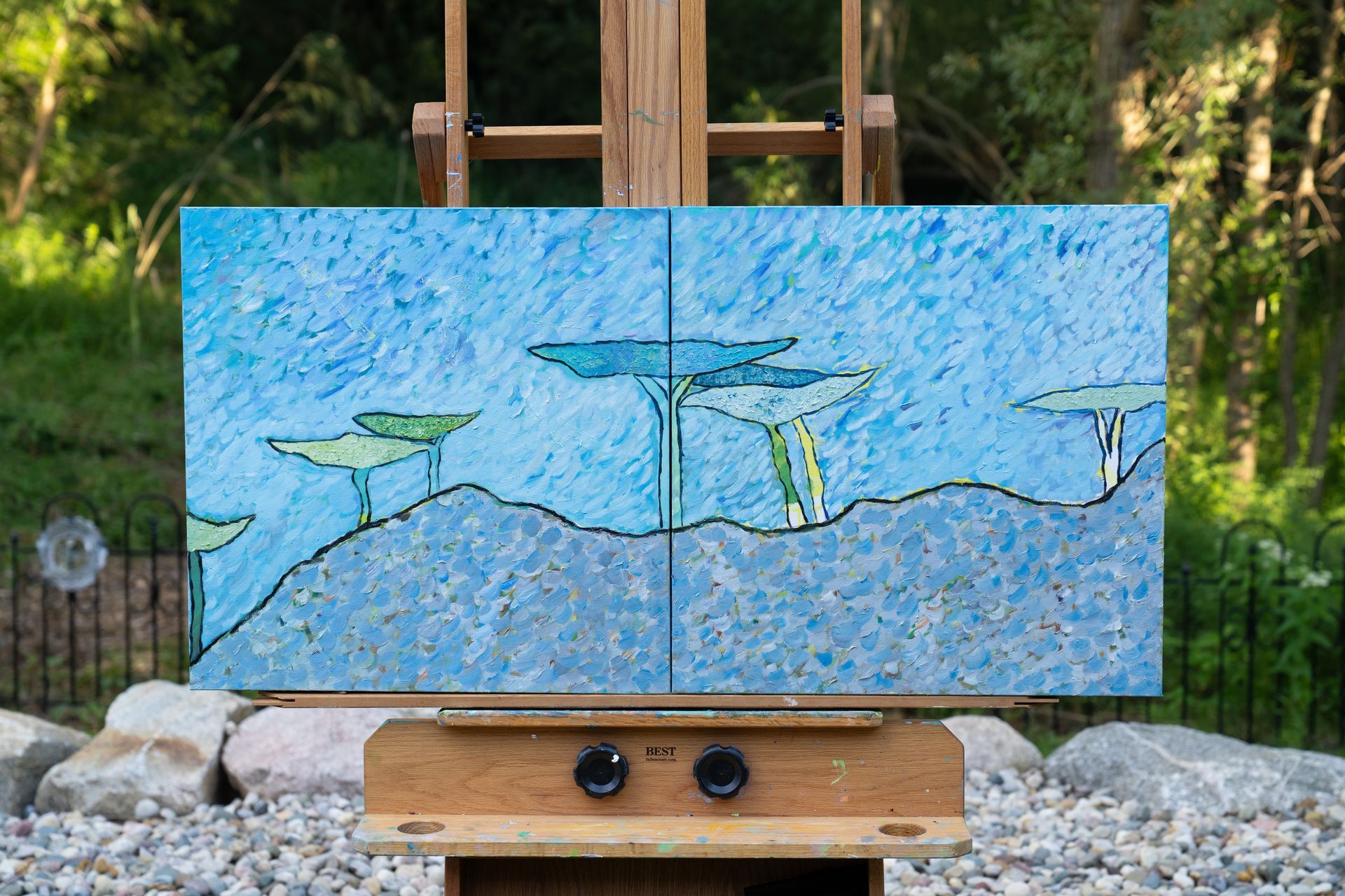 Two-panel painting on an easel featuring blue sky and stylized trees against a textured background.