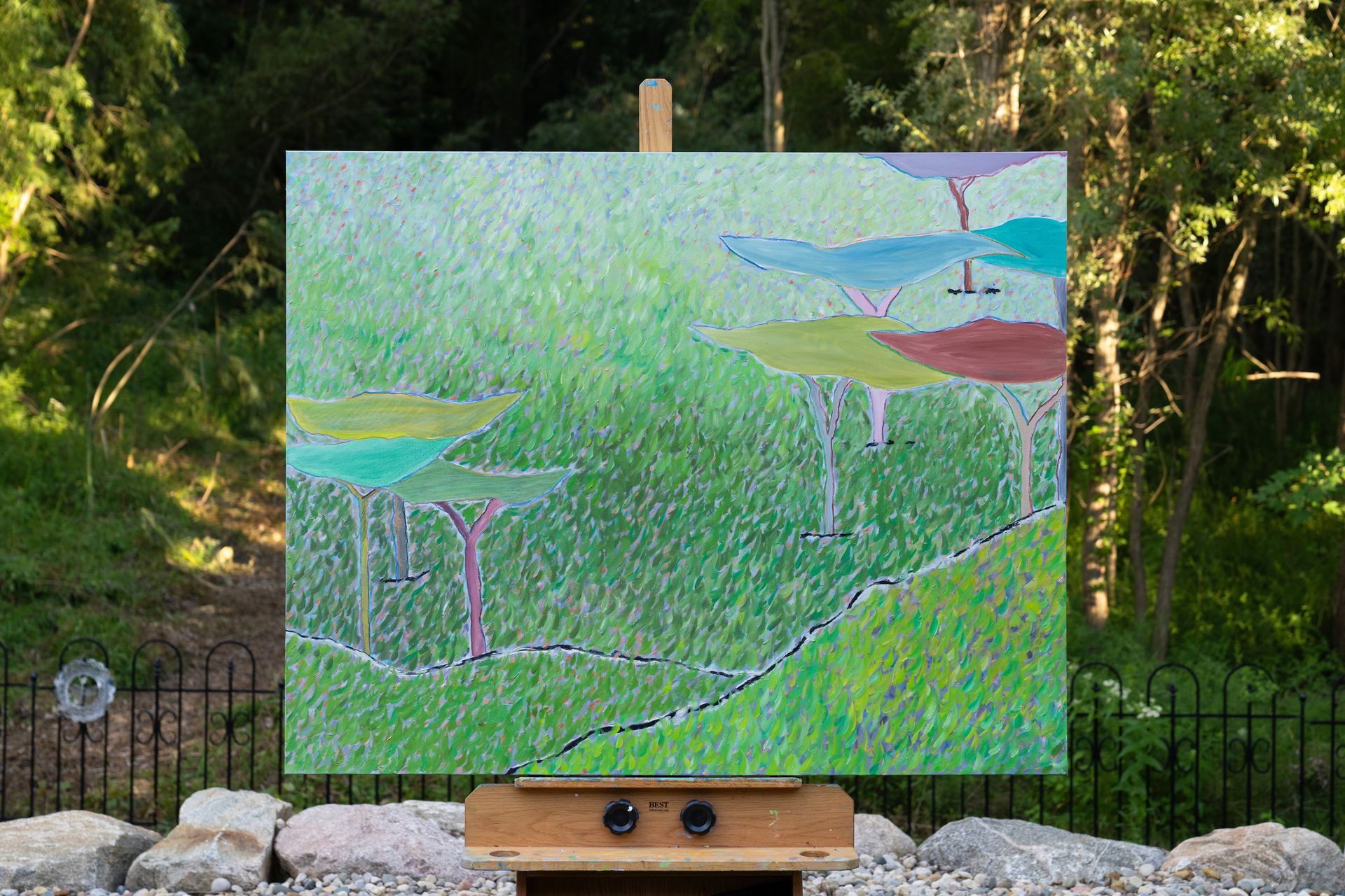 Painting on an easel outdoors. Fantasy landscape in green, blue, and brown; trees and ground.
