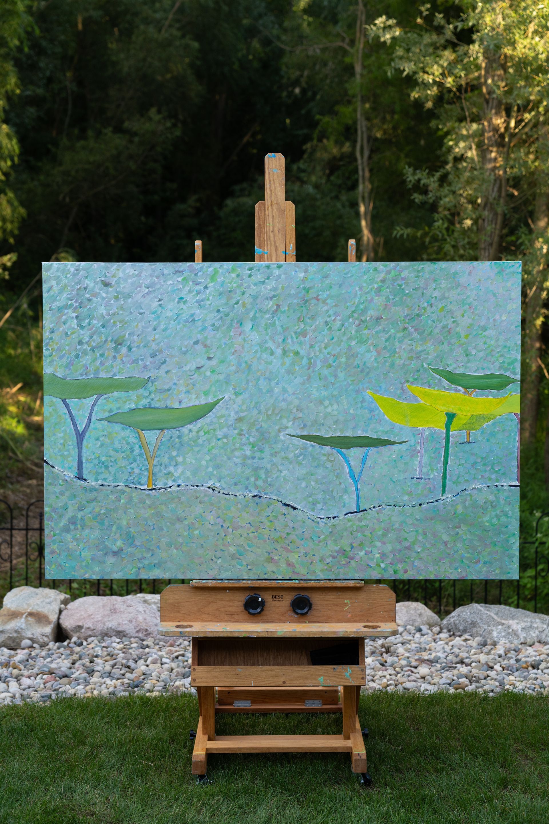 Painting of water lilies in a turquoise pond displayed on a wooden easel outdoors.